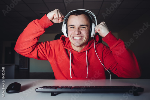 Joyful young man with headphones at home playing a computer game. Gamer happy for the win. photo