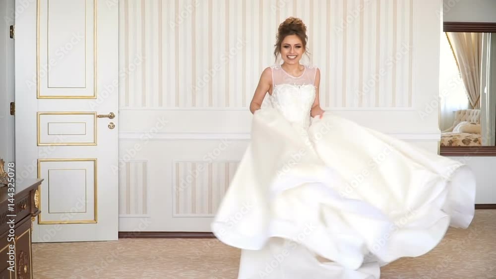 Portrait of beautiful young bride. A girl is posing in a hotel room. The lady is spinning in her wedding dress Portrait of beautiful young bride. A girl is posing in a hotel room. The lady is spinning in her wedding dress