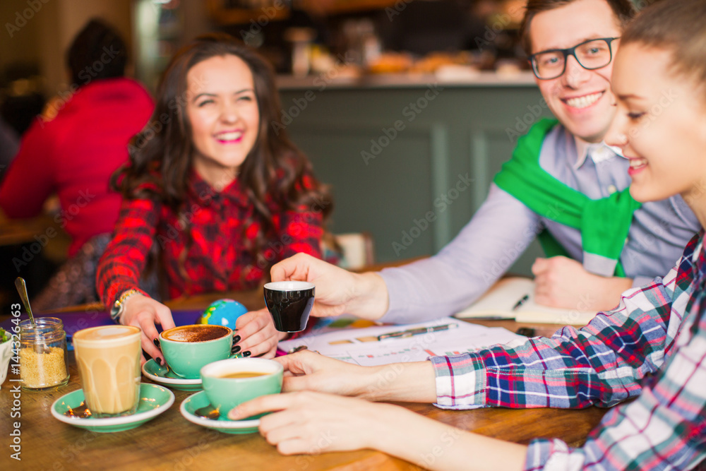 Smiling people sit at the table with cups of coffee in time of break, in a cafe Smiling people sit at the table with cups of coffee in time of break, in a cafe