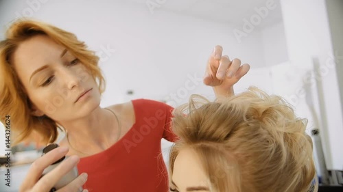 Female hairdresser of luxury beauty salon is standing and working with young blonde model