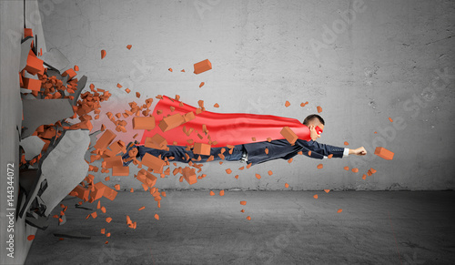 Fotografia A superhero businessman in a cape flying right through the wall leaving rubble behind him