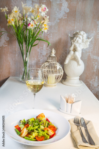 Vegetable salad with tomatoes and shrimps on the table in a composition with a glass of wine