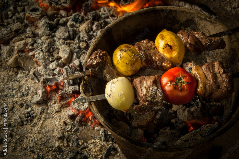 pieces of meat with tomato and lemon cooked on burning coals. the dish is cooked and smoked on charcoal
