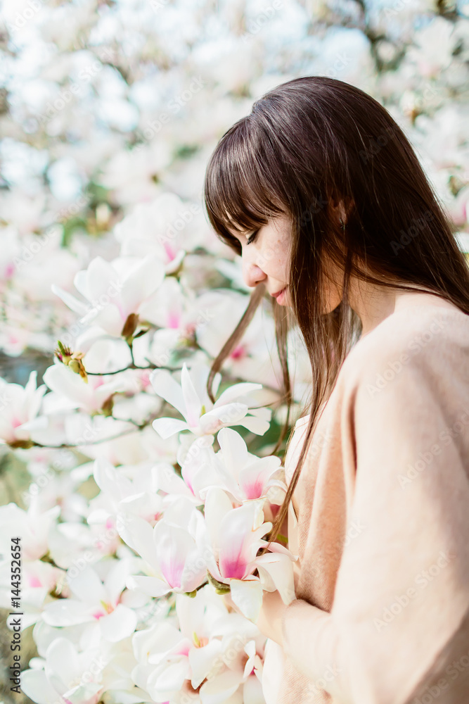 Beautiful brunette woman and white magnolia in park. Spring time Beautiful brunette woman and white magnolia in park. Spring time