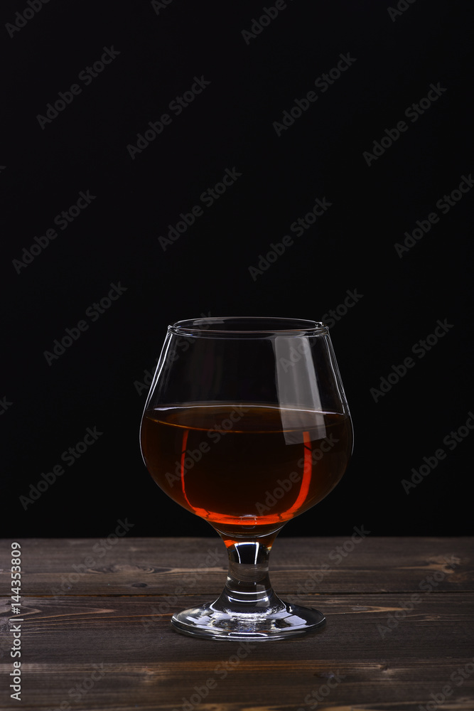 glass with cognac or whiskey on black wooden table glass with cognac or whiskey on black wooden table
