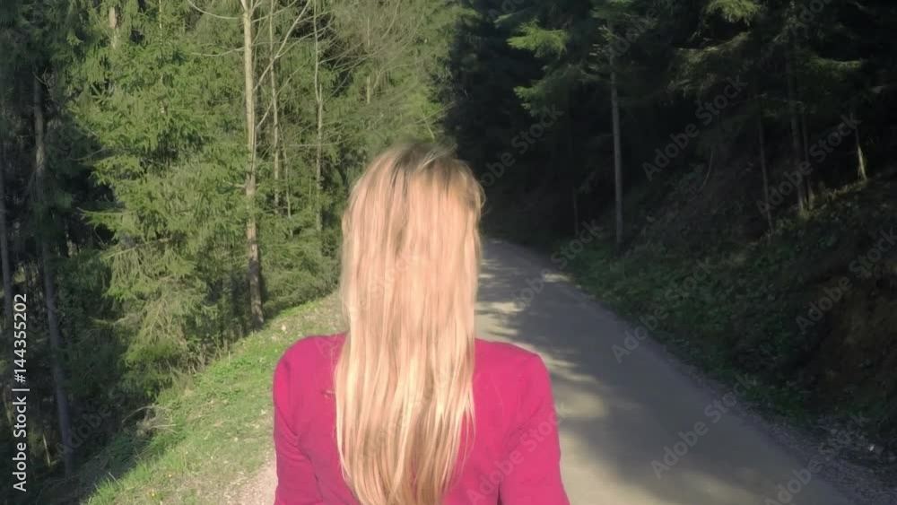Long hair woman walks alone on the sunny forest road. Slow motion.
