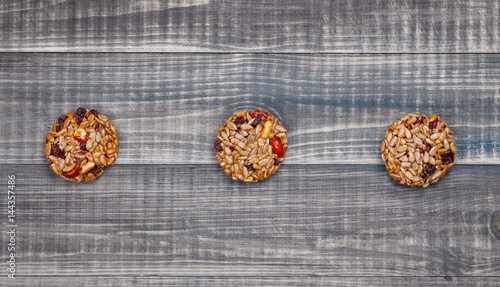 Three sweets lie on a gray wooden table in a row. Sweets consists of seeds, nuts, raisins with honey.