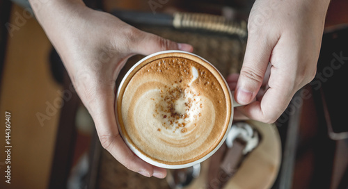 Hands holding on hot latte coffee mug.