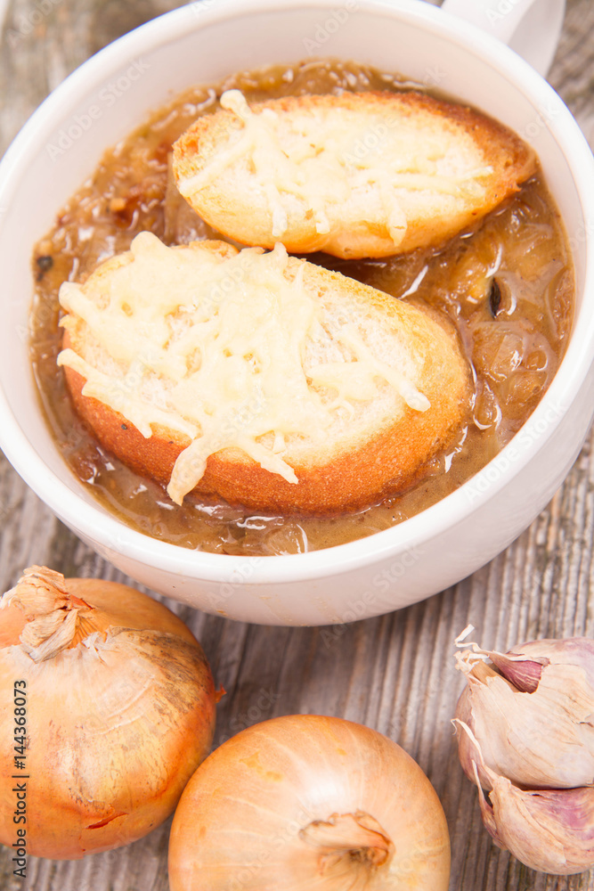Onion soup with toast on a wooden background with some onions and garlic Onion soup with toast on a wooden background with some onions and garlic