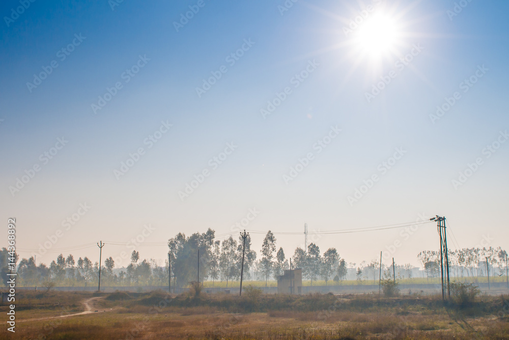 Traveling by train in India. View from an opened train door with a colorful landscape, morning fog and shining sun in the blue sky.