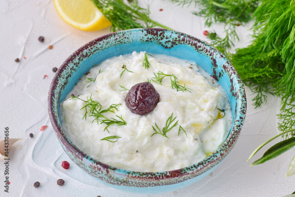 Homemade Greek traditional sauce tzatziki with cucumber, garlic, yogurt , olive oil and lemon in a traditional colored bowl on a white background. Healthy eating concept. Mediterranean lifestyle Homemade Greek traditional sauce tzatziki with cucumber, garlic, yogurt , olive oil and lemon in a traditional colored bowl on a white background. Healthy eating concept. Mediterranean lifestyle