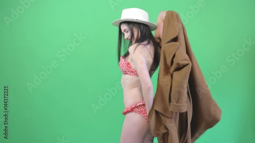 Attractive young woman opens coat and shows bikini. Greenscreen