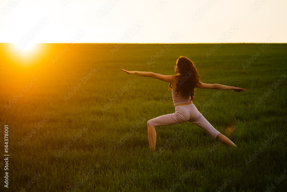 Young woman doing complex Yoga exercise on green lawn at sunset