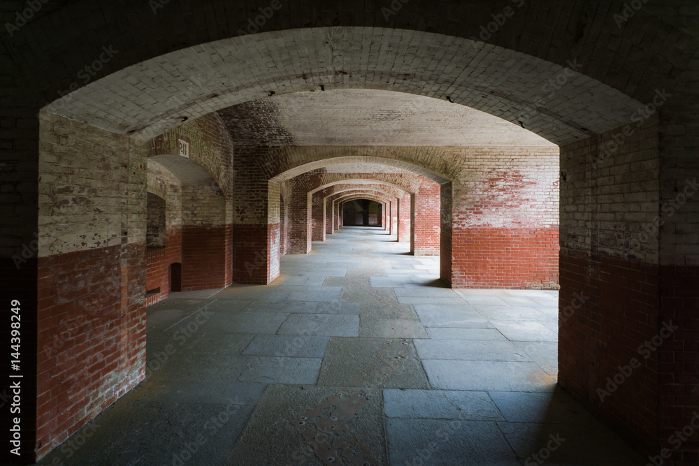 Masonry arched hallway stretching away into the darkness. Typical of forts and prisons of the Victorian period