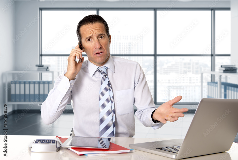 angry senior businessman in stress working and talking on mobile phone at computer desk