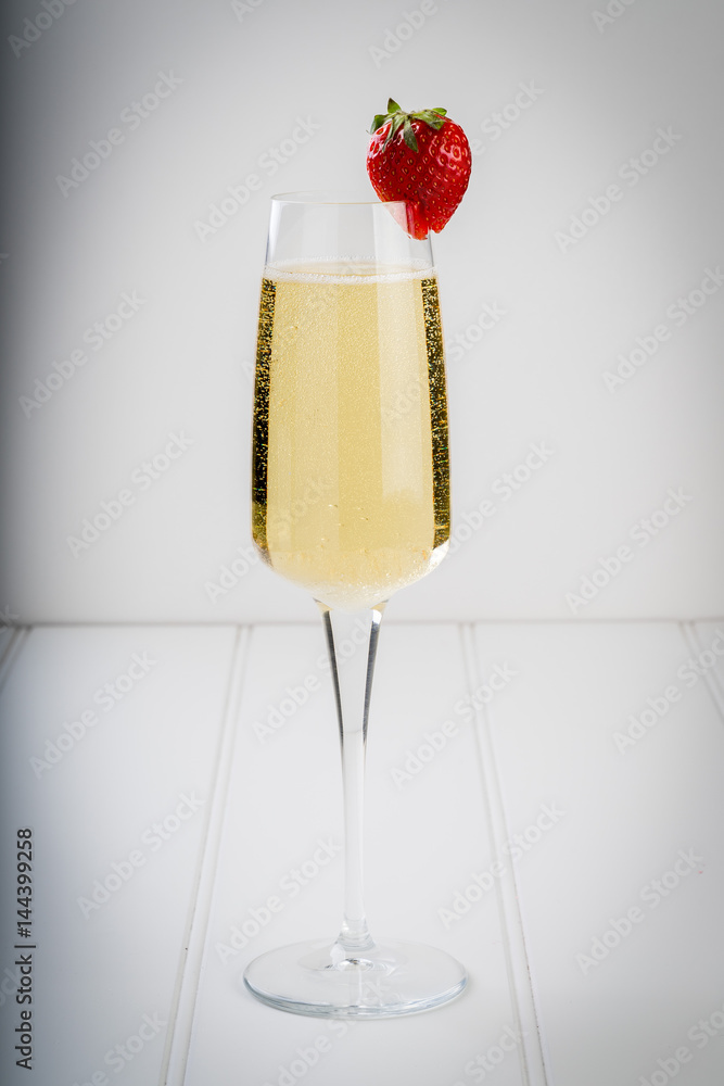 champagne sparkling white wine glass and bottle on plain background with strawberry garnish gold ribbon