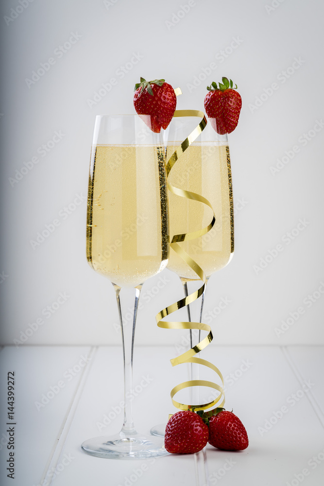 champagne sparkling white wine glass and bottle on plain background with strawberry garnish gold ribbon