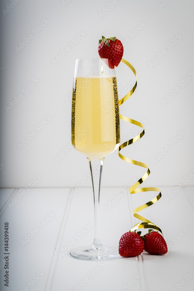 champagne sparkling white wine glass and bottle on plain background with strawberry garnish gold ribbon