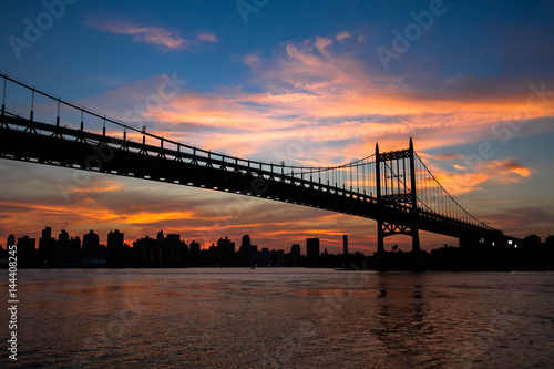 Triborough bridge over the river and buildings in silhouette and sunset sky