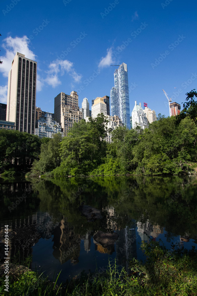 Fototapeta premium Reflective lake under the shade and buildings in Manhattan