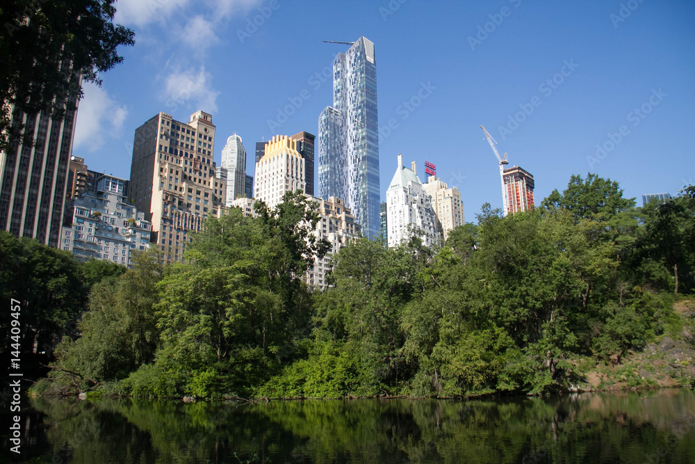 Fototapeta premium Reflective lake under the shade and buildings in summertime, Manhattan