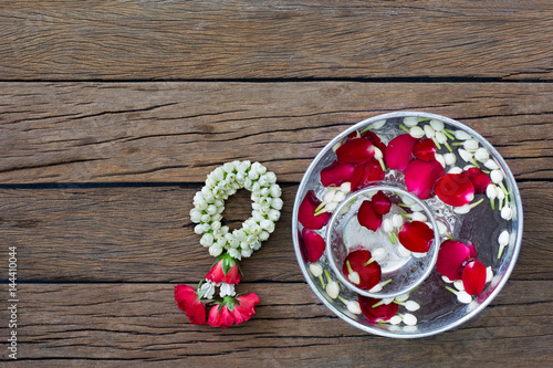 Water bowl with petal flowers and garland on old wooden table in Songkran festival