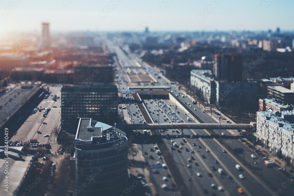 True tilt shift shooting of highway in metropolis from high point: multiple residential and office buildings, parking, many cars on busy streets of the city, crosstown traffic, sunny springtime