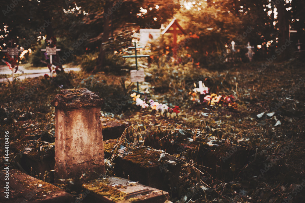Old cracked mossy tombstone on graveyard with orthodox crosses above tombs in blurred background on moody autumn morning with copy space for your text message