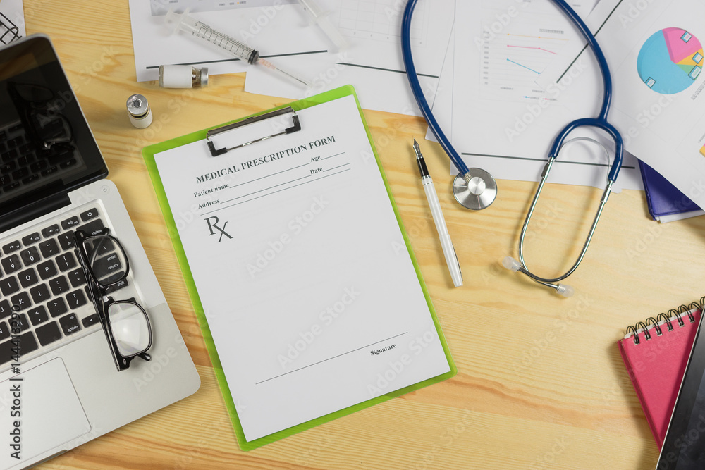 Top view of modern, sterile doctors office desk. Medical accessories,stethoscope laptop pen syring and vaccineprescription with copy space around products.clip board, glasses and other things Top view of modern, sterile doctors office desk. Medical accessories,stethoscope laptop pen syring and vaccineprescription with copy space around products.clip board, glasses and other things