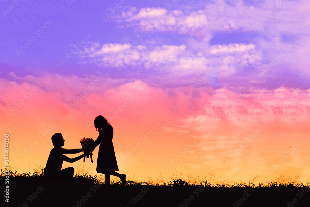 Proposal with a man silhouette asking for marry at sunset with the sun in the background, boquet of flowers kneeling and give engagement ring for his girlfriend