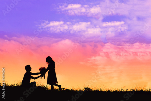 Proposal with a man silhouette asking for marry at sunset with the sun in the background, boquet of flowers kneeling and give engagement ring for his girlfriend © Have a nice day 