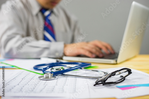 Stethoscope with clipboard and Laptop on desk,Doctor working in hospital writing a prescription, Healthcare and medical concept,test results in background,vintage color,selective focus