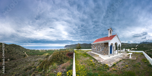 Scenic landscape with the church Agios Nektarios on a hill and aegean sea on a dramatic cloudy day, Milatos, Crete, Greece.