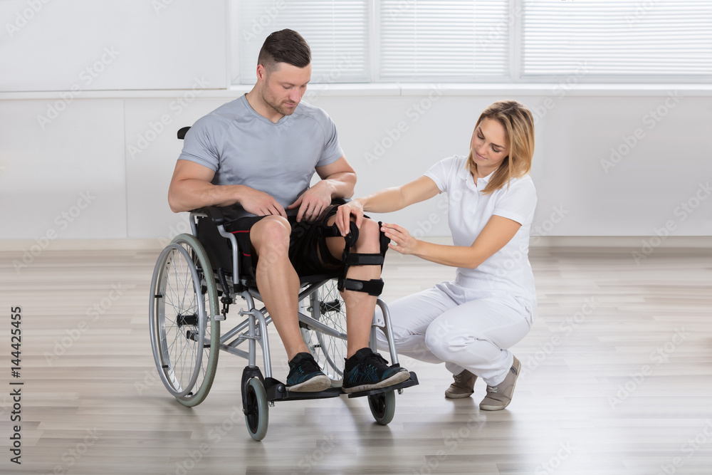 Female Physiotherapist Fixing Knee Braces On Man's Leg Female Physiotherapist Fixing Knee Braces On Man's Leg
