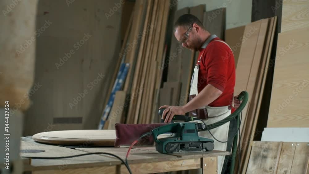 Carpenter with various electric sanders polishing a round plank in workshop Carpenter with various electric sanders polishing a round plank in workshop