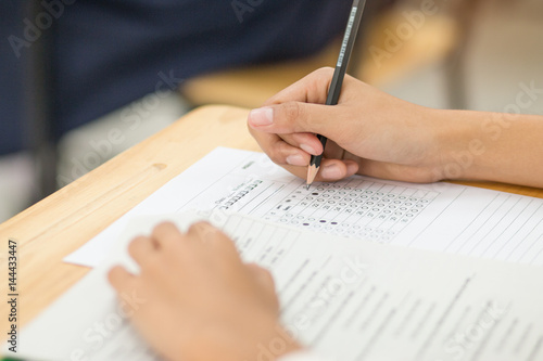 students hand holding pencil fill in Exam carbon paper sheet or test paper multichoice on wood desk, education concept