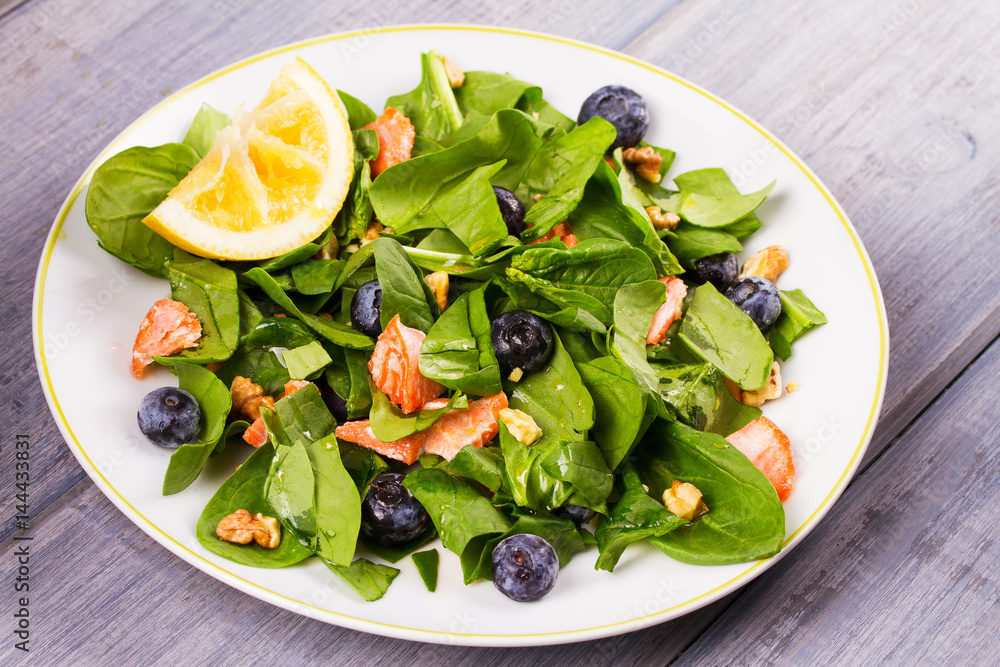 Spinach, salmon, blueberries and walnuts salad on white plate