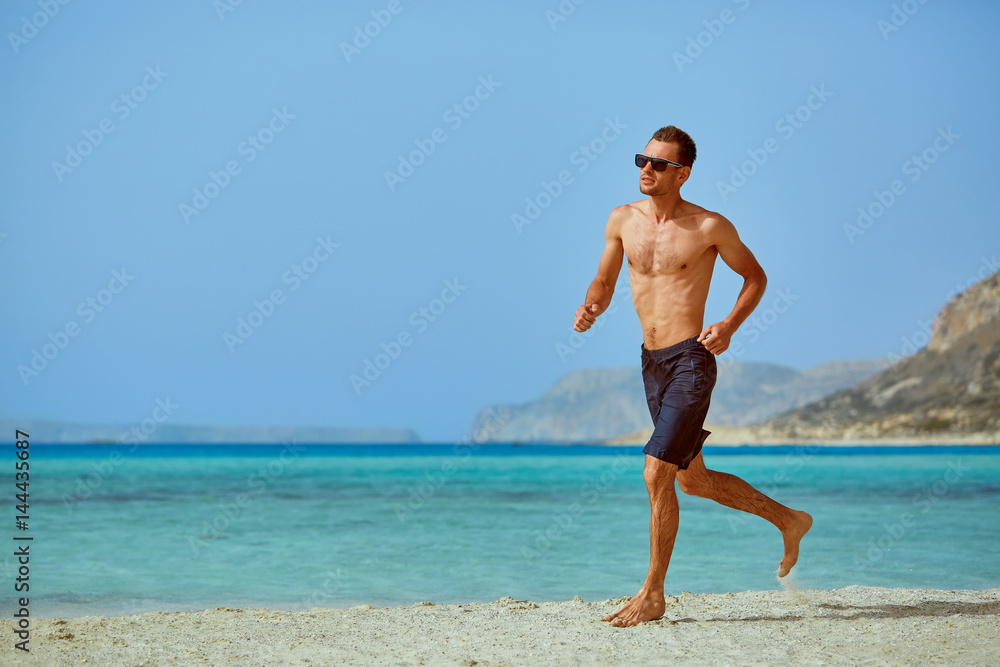 strong athletic man with bared torso running on the beach along the sea front