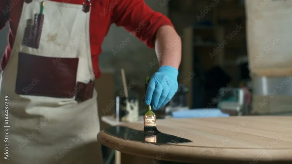 Carpenter in gloves painting the table with a black dye in the workshop Carpenter in gloves painting the table with a black dye in the workshop