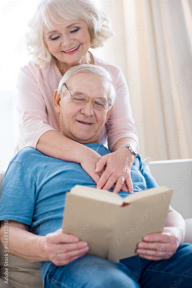 Happy senior couple hugging and relaxing, man reading book Happy senior couple hugging and relaxing, man reading book