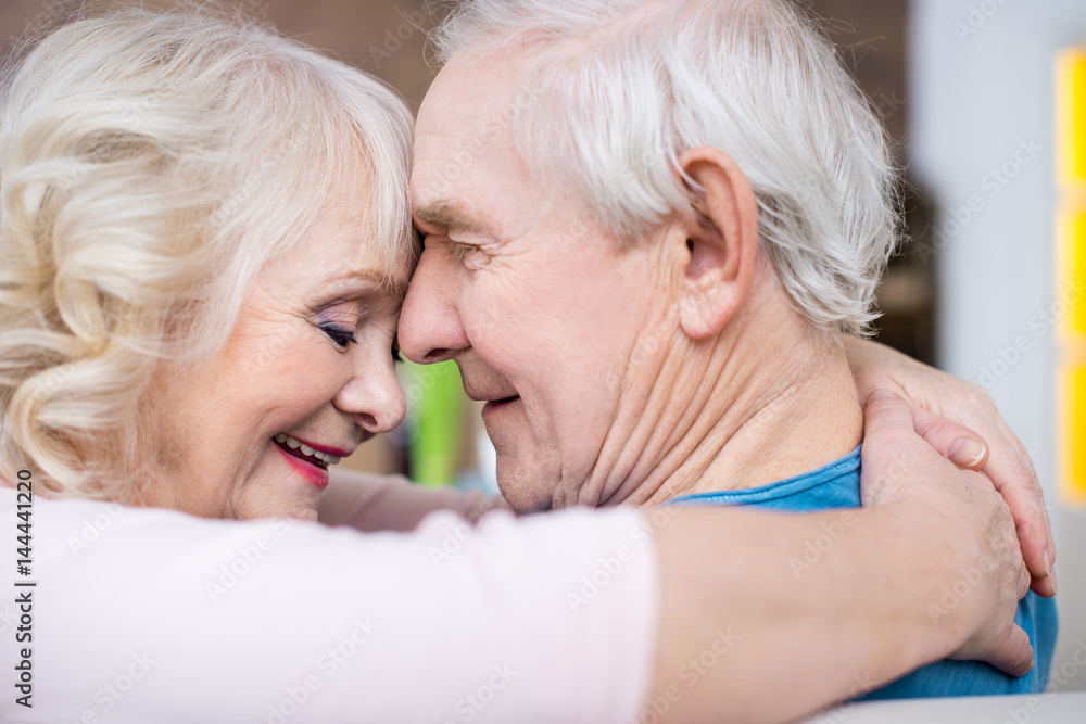 Happy senior couple embracing and touching foreheads at home Happy senior couple embracing and touching foreheads at home