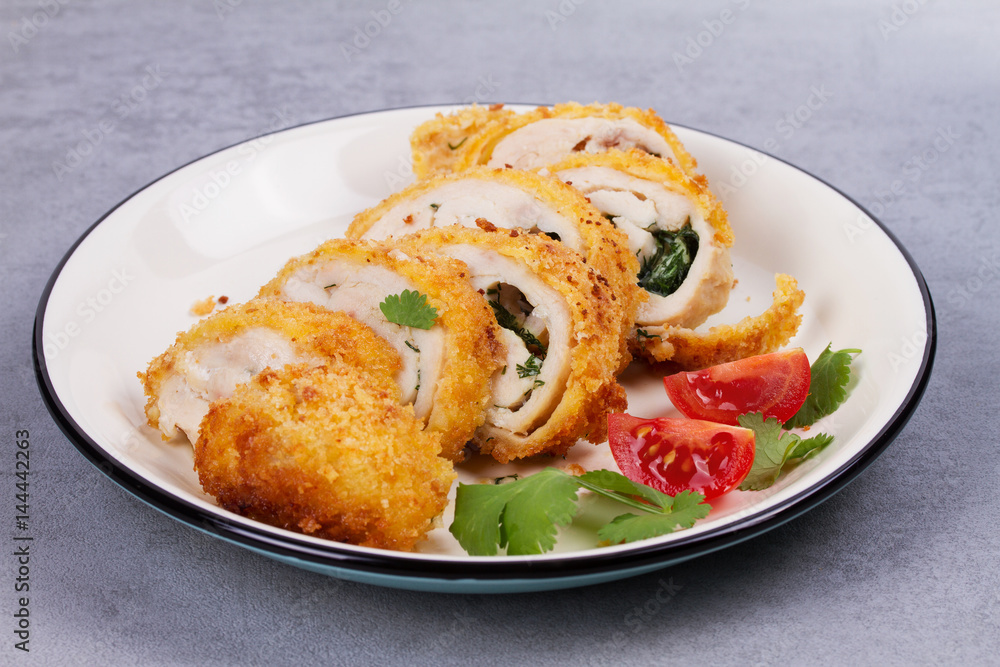 Chicken Kiev garnished with cilantro and tomatoes. Breaded chicken breast stuffed with herbs and butter on white plate Chicken Kiev garnished with cilantro and tomatoes. Breaded chicken breast stuffed with herbs and butter on white plate