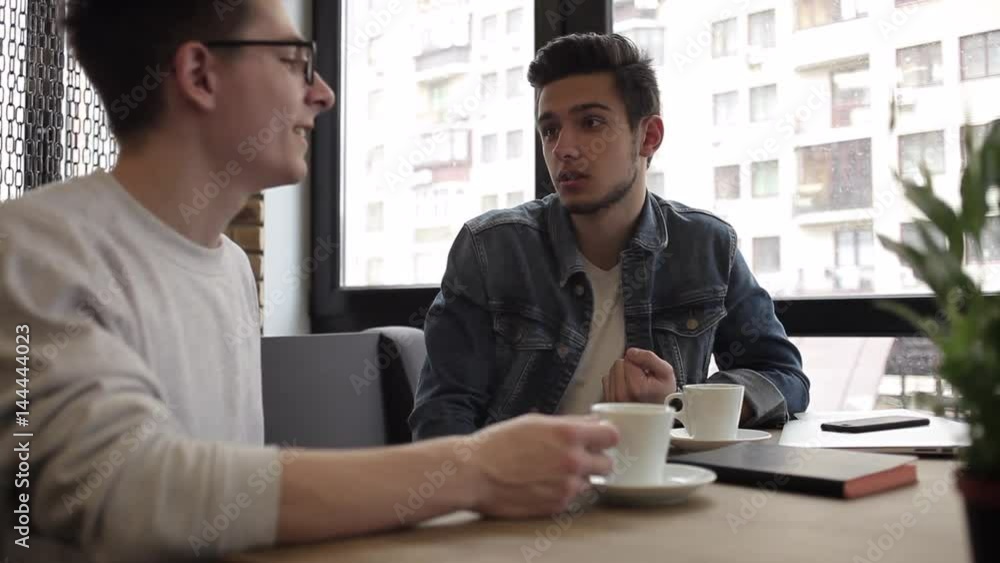 Two buddies sitting in the cafe and chatting with each other Two buddies sitting in the cafe and chatting with each other