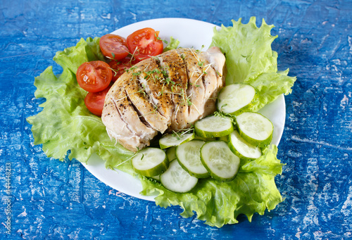 Chicken breast with herbs, tomatoes and cucumbers on blue background