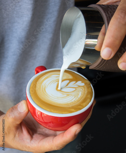 Vertical image of pouring milk to espresso coffee make latte art on red cup coffee