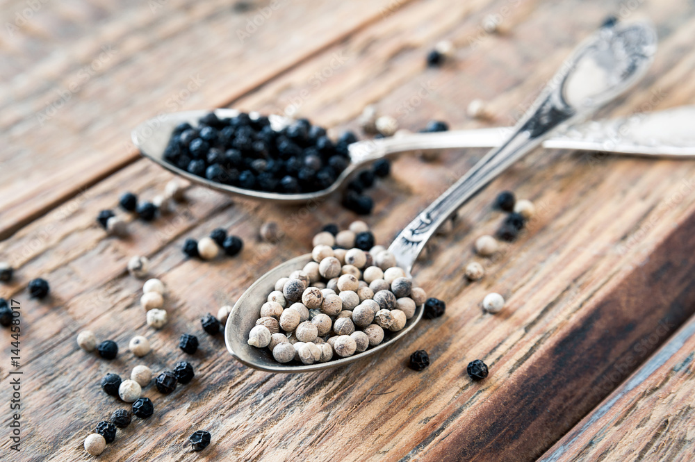 Mix of spices, peppercorns. Two metalic crossed teaspoons with black and white dried pepper grains on old vintage wooden table background. Closeup. Mix of spices, peppercorns. Two metalic crossed teaspoons with black and white dried pepper grains on old vintage wooden table background. Closeup.