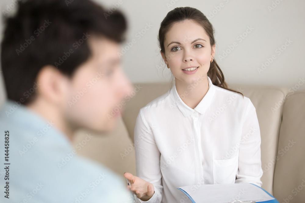 Young female psychotherapist wearing white shirt encouraging and cheering up frustrated male patient, suffering from depression, looking indifferent. Psychological counseling of woman-therapist Young female psychotherapist wearing white shirt encouraging and cheering up frustrated male patient, suffering from depression, looking indifferent. Psychological counseling of woman-therapist