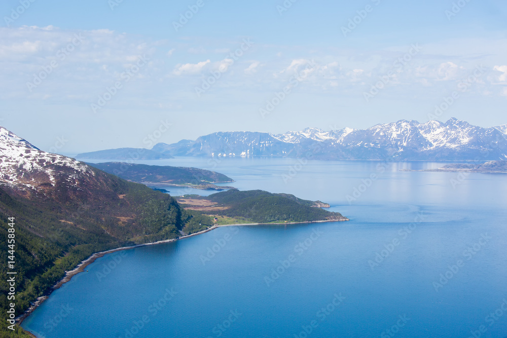 Northern Norway's countryside landscape of snowy and rocky mountains, aqua blue sea, and seaweed beach, during spring season