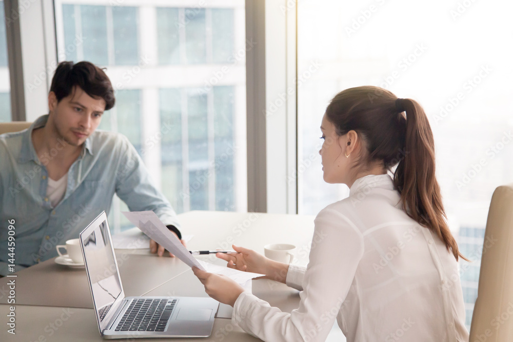 Obraz premium Businessman and businesswoman discussing business issues using laptop and looking through papers. Young woman showing documents to male colleague, man is serious and thinking how to solve a problem