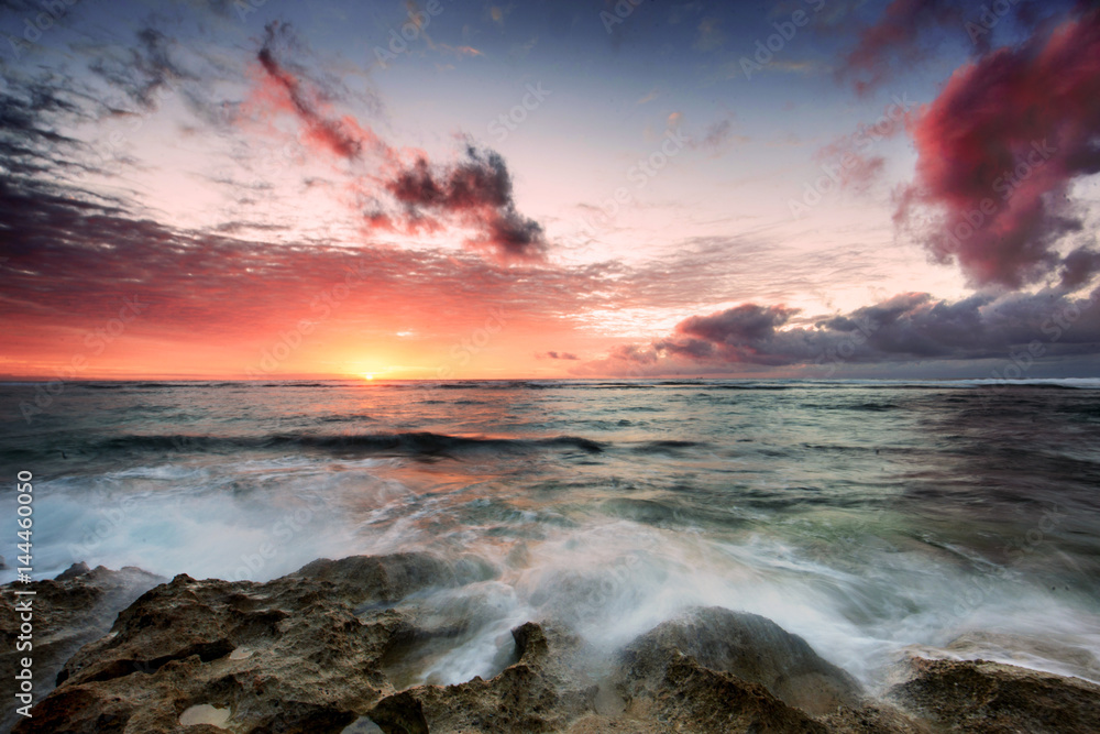 Cloudy sunset over horizon, waves crashing over rocks